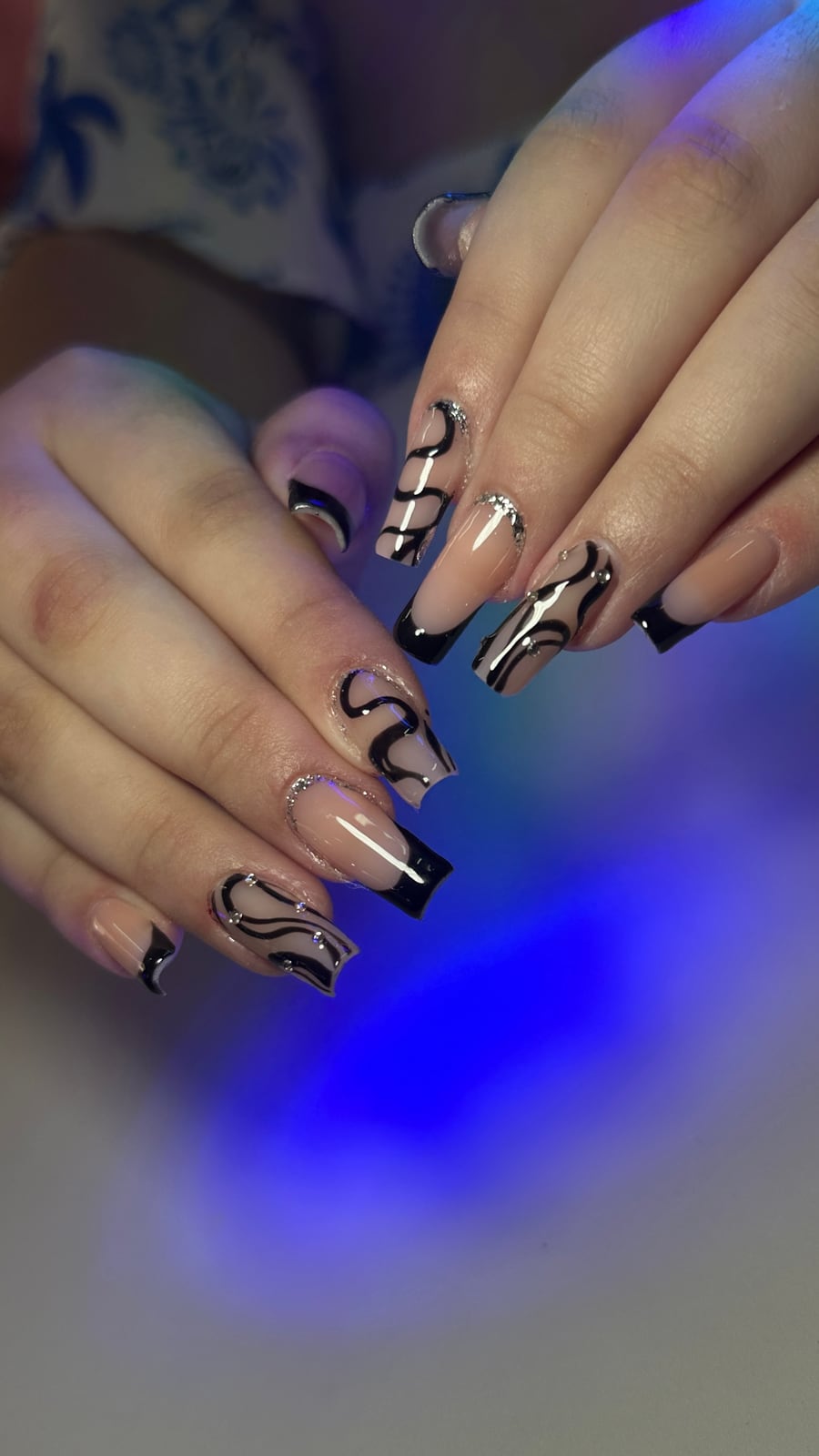 Unhas longas decoradas com traços pretos e pequenos detalhes brilhantes.